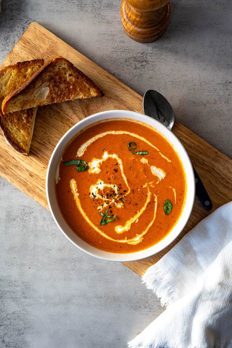 bowl of tomato soup with a halved grilled cheese on a wooden board.