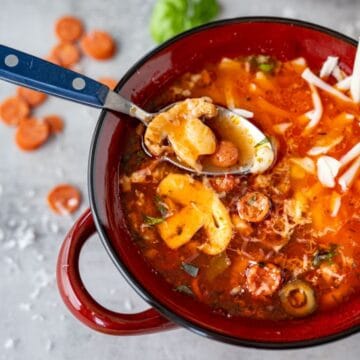 bowl of pizza soup topped with shredded mozarella with a blue spoon.