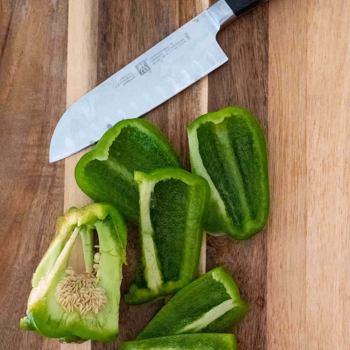 green bell pepper cut into chunks on a wooden cutting board.