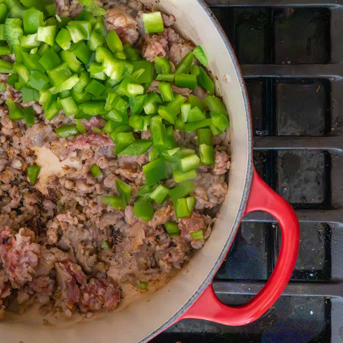browned Italian sausage and diced green pepper with a small amount of chicken broth in a red dutch oven.
