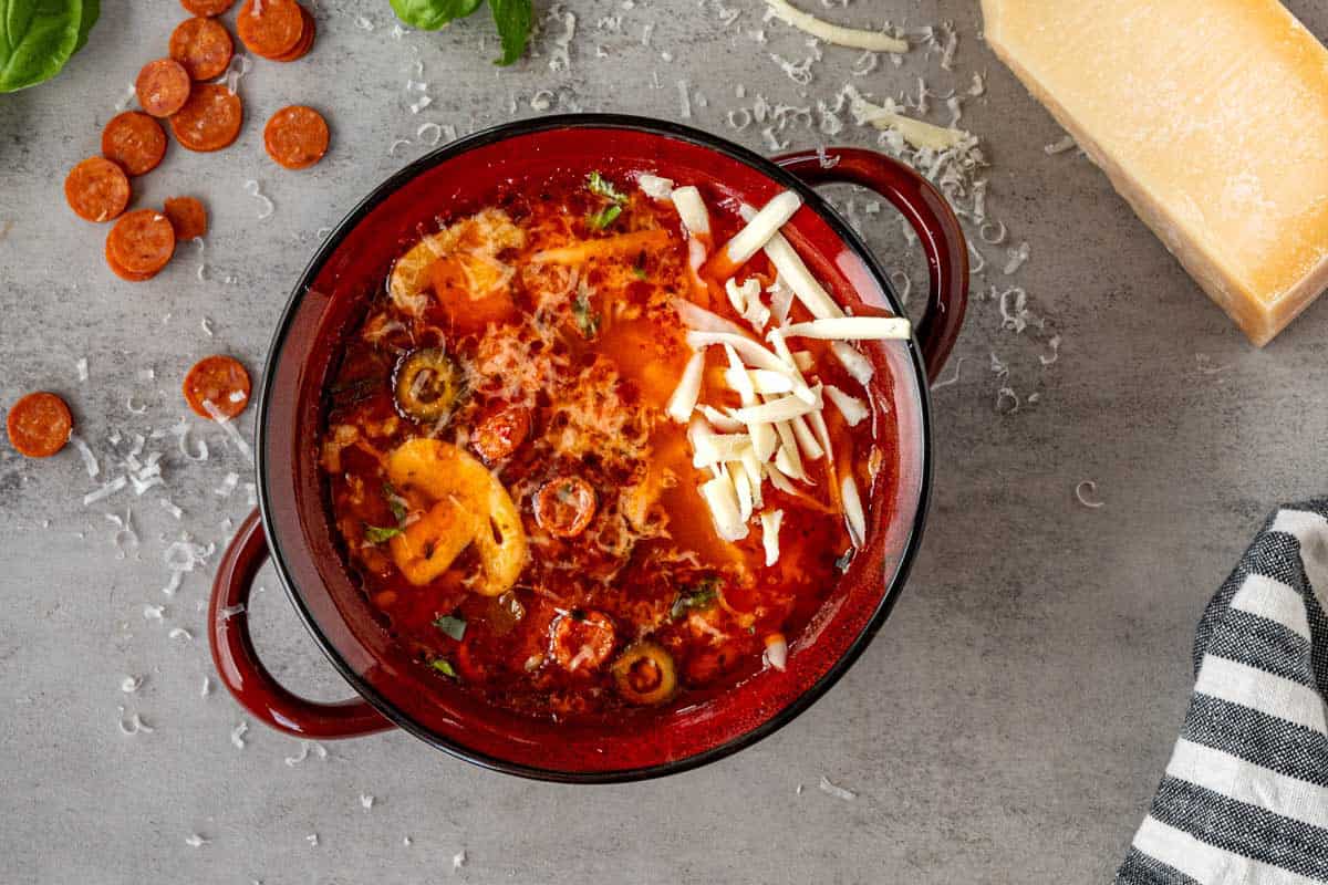 red bowl of pizza soup topped with cheese.