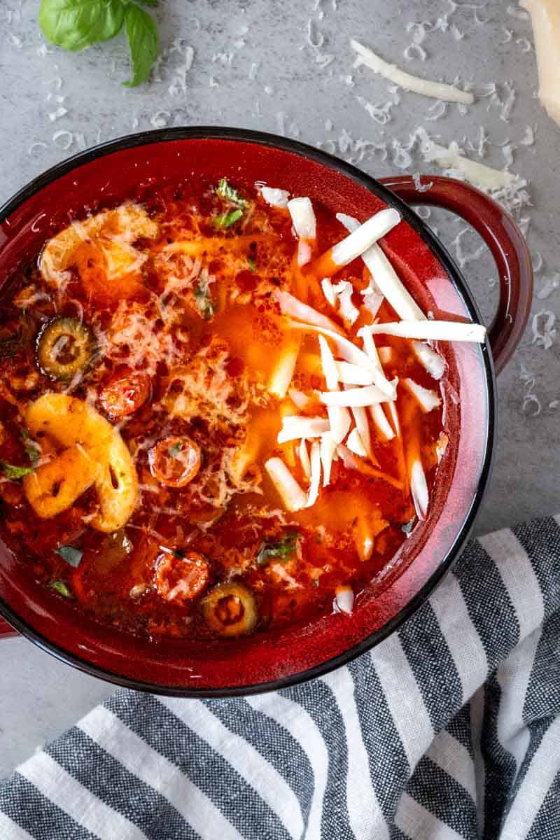 close up of a bowl of pizza soup topped with shredded cheese.