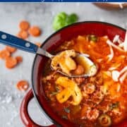 Spoonful of pizza soup showing pepperoni, sausage, peppers, and tomato broth inside a red soup pot.