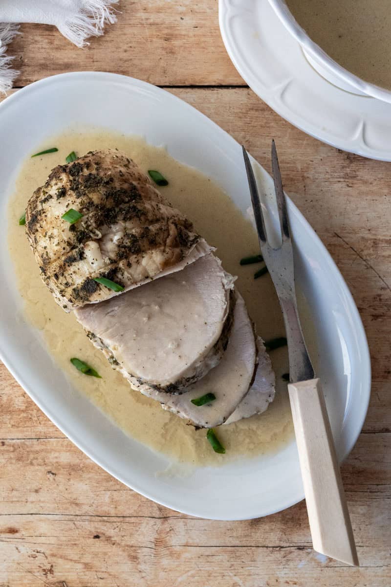 platter of sliced turkey breast covered with gravy alongside a gravy boat with extra gravy inside.