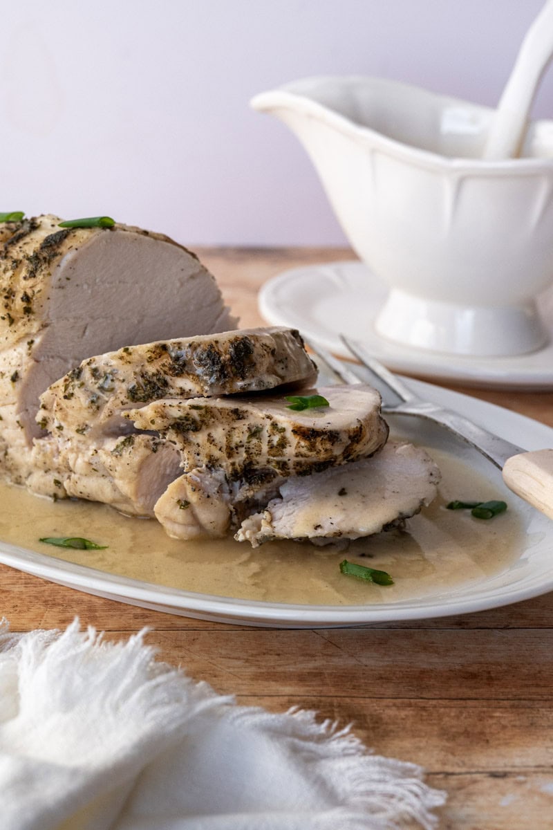 sliced turkey breast on a white platter covered in gluten free gravy.