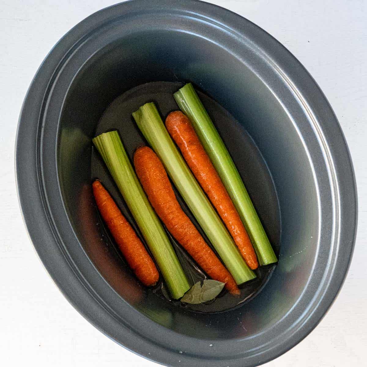 in the bottom of a slow cooker is whole carrots and celery stalks.