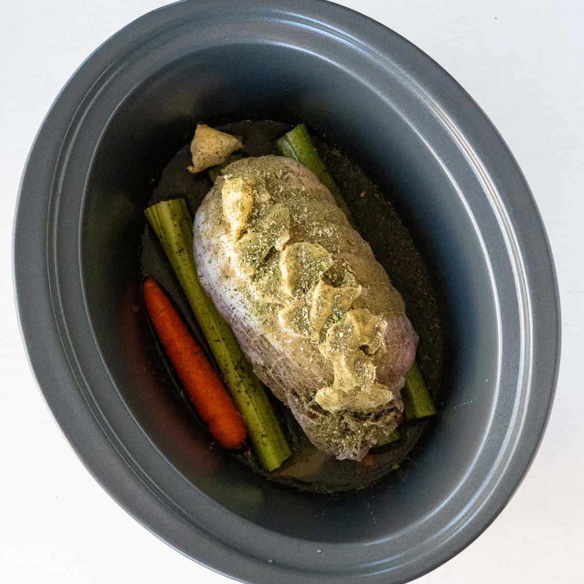 butter topped turkey breast sitting in a slow cooker with spices sprinkled over it.