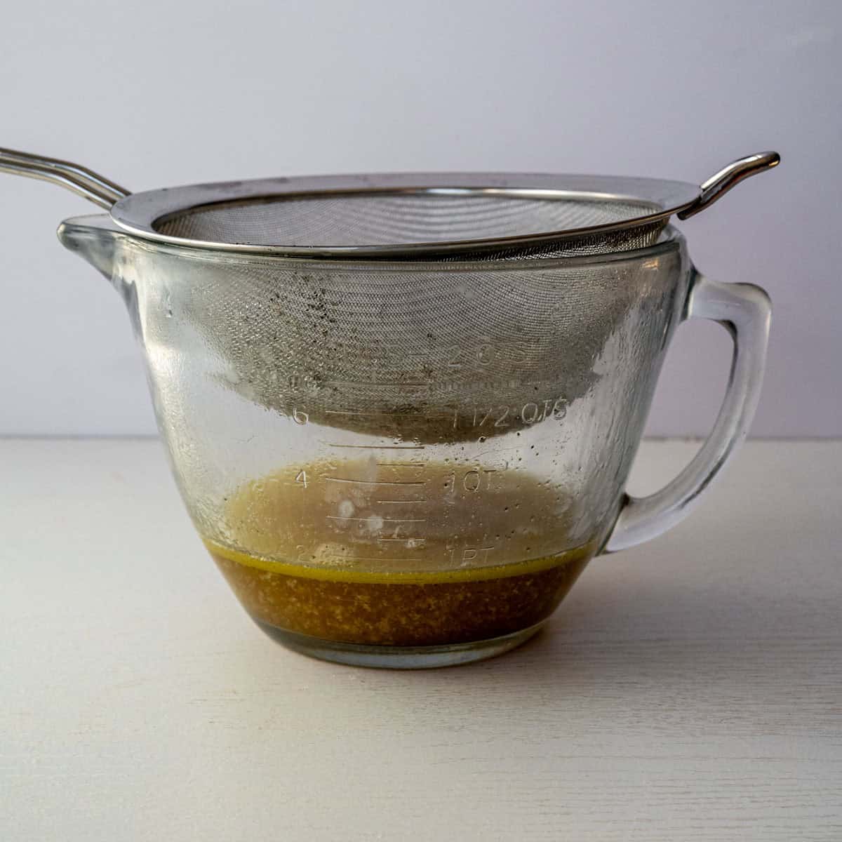 large glass bowl with a mesh strainer on top catching the turkey drippings.