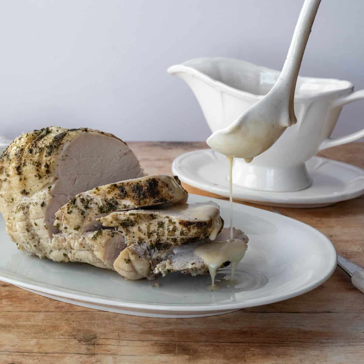 pouring gravy over sliced turkey breast on a platter.