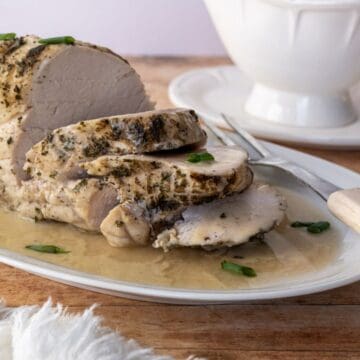 sliced turkey breast on a white platter with gravy.
