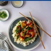 plate of chicken stir fry on a plate with white rice and chop sticks.