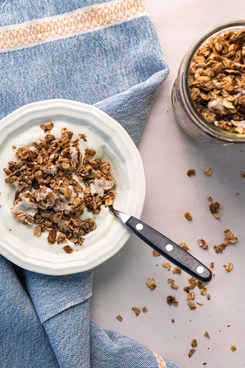 bowl of yogurt topped with cinnamon roll granola next to a mason jar full of granola.