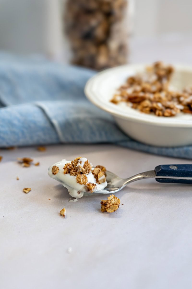 spoonful of yogurt and granola in front of a bowl and a mason jar full of granola.