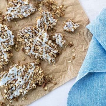 clusters of cinnamon roll granola on a piece of parchement paper next to a blue napkin.
