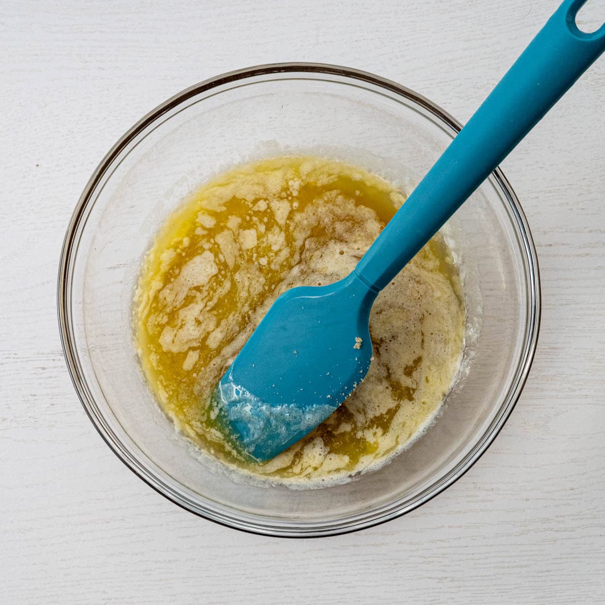 glass bowl with the wet ingredients and a blue spatula.