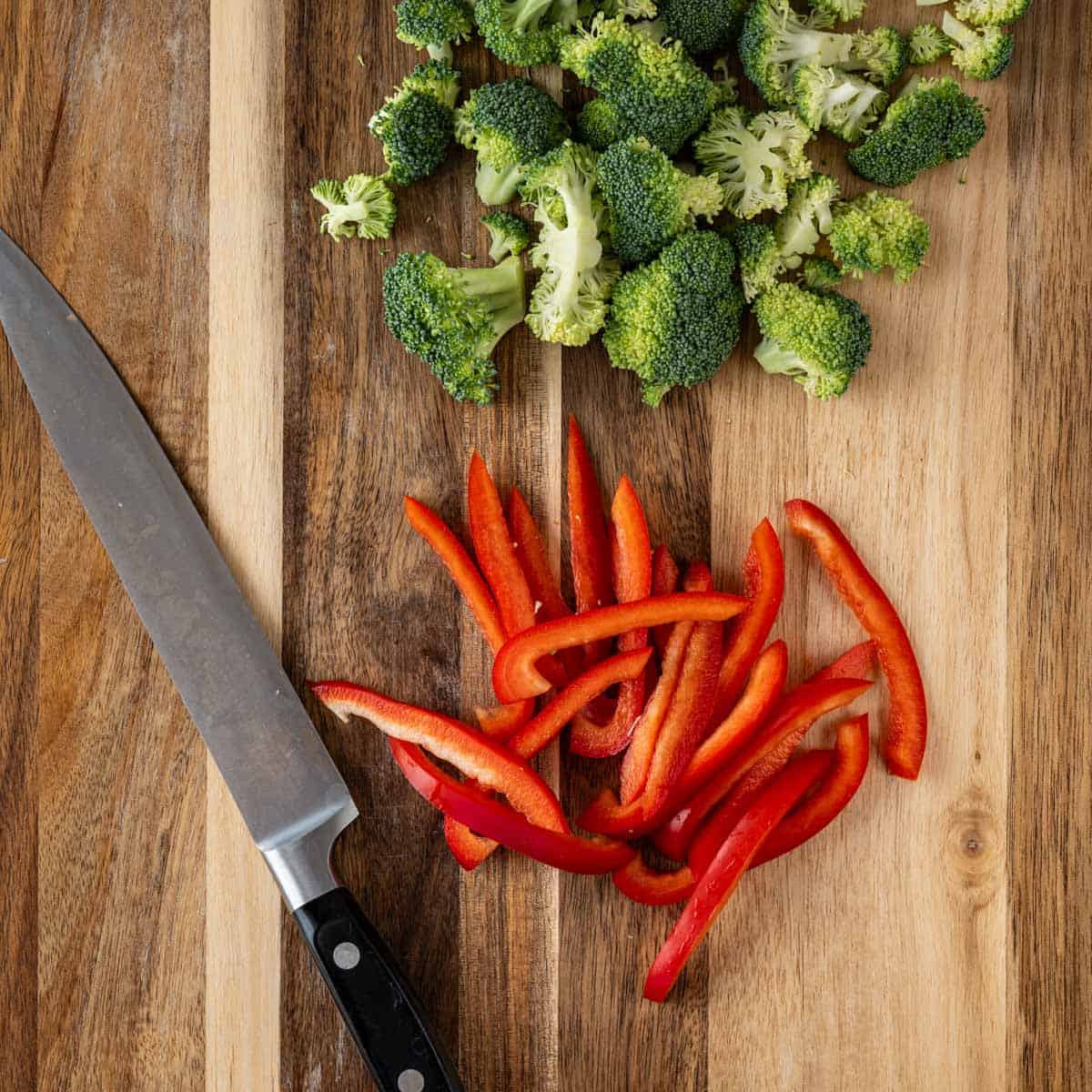 chopped broccoli florets and red bell pepper strips on a wooden cutting board.