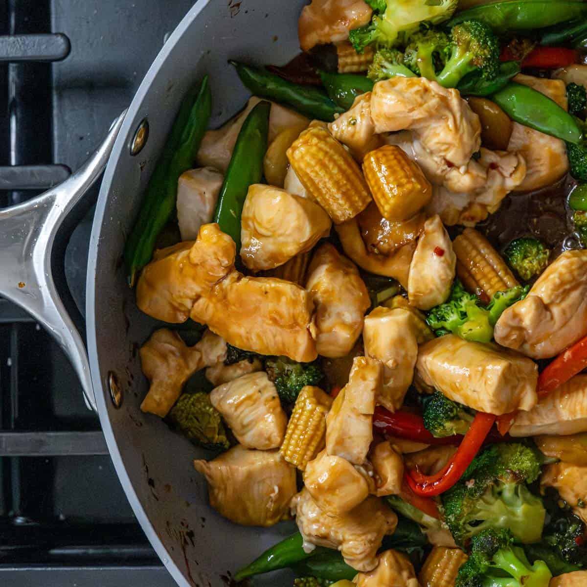cooked chicken, vegetables covered in stir fry sauce in a large skillet.