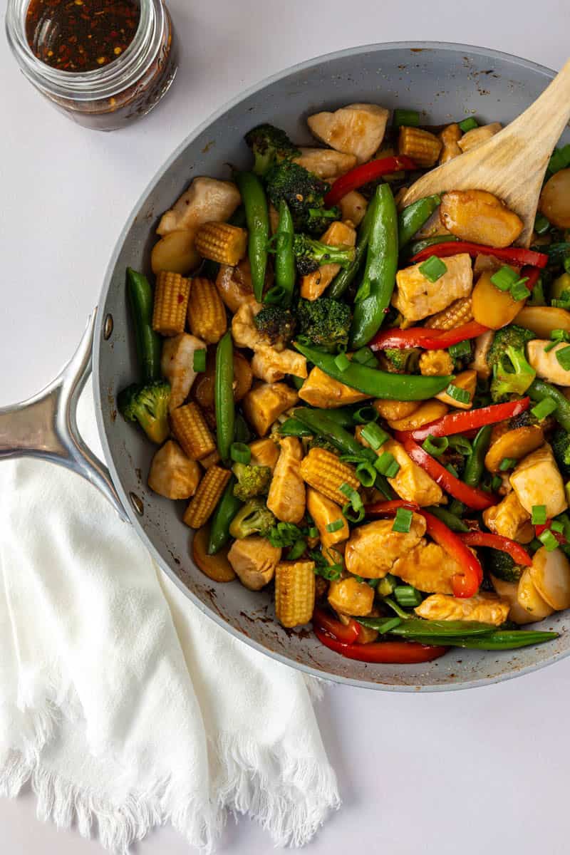 large skillet of chicken stir fry with a wooden spoon. 