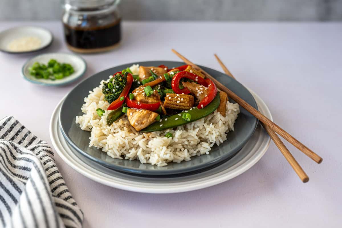 plate of chicken stir fry with chop sticks with a jar of extra sauce and toppings in the background.