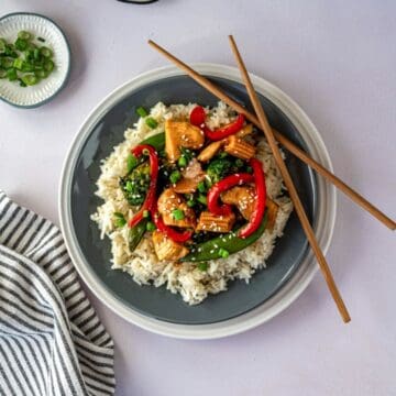 chicken stir fry on a bed of white rice on a plate with chop sticks.