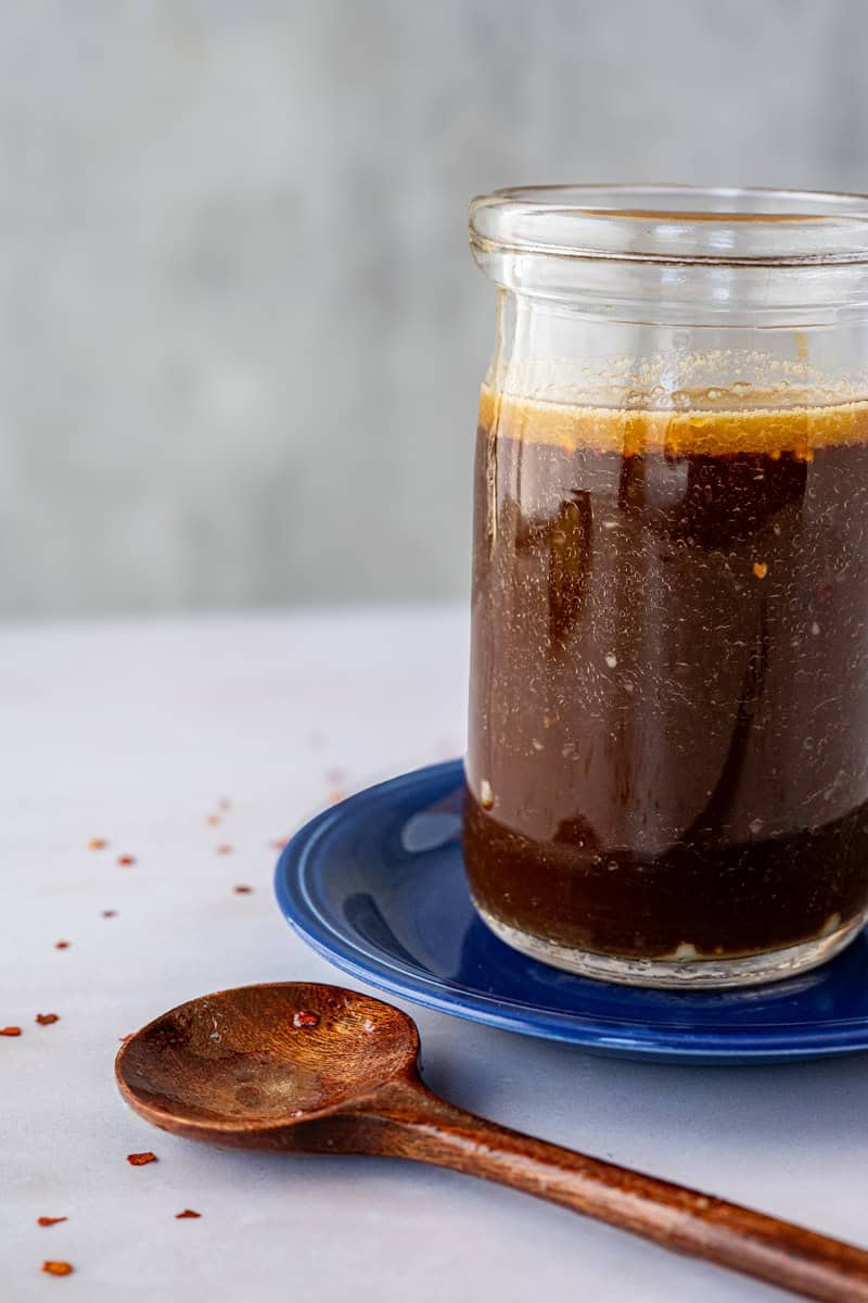 stir fry sauce in a mason jar on a blue plate alongside a small wooden spoon.