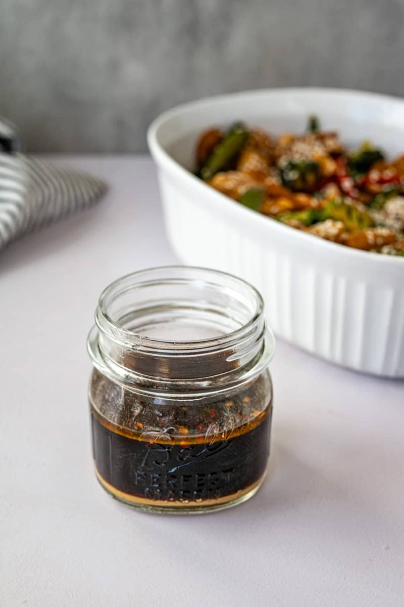 mason jar of stir fry sauce alongside chicken stir fry.