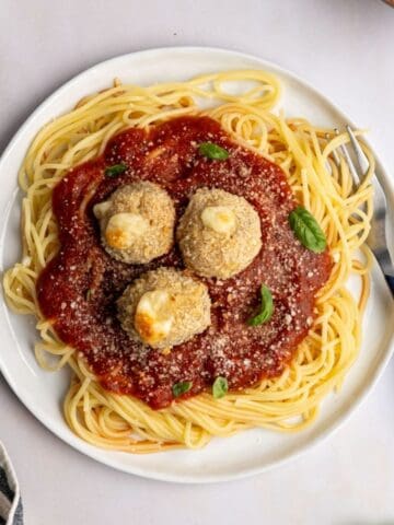 plate of spaghetti noodles topped with sauce and three crispy chicken parmesan meatballs topped with grated parm cheese and fresh basil.
