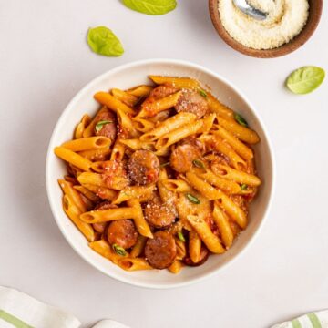 overhead shot of kielbasa pasta in a bowl topped with grated parmesan cheese and fresh basil.