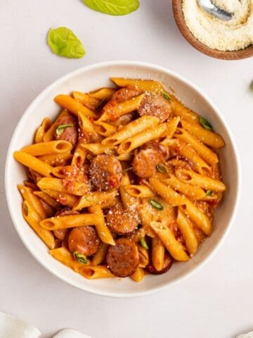 overhead shot of kielbasa pasta in a bowl topped with grated parmesan cheese and fresh basil.