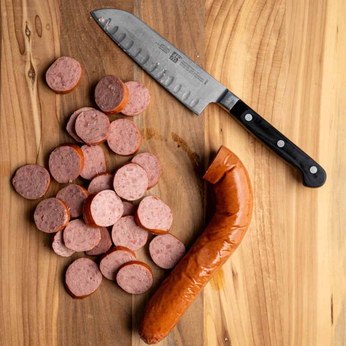 sliced kielbasa rounds on a wooden cutting board with a knife.