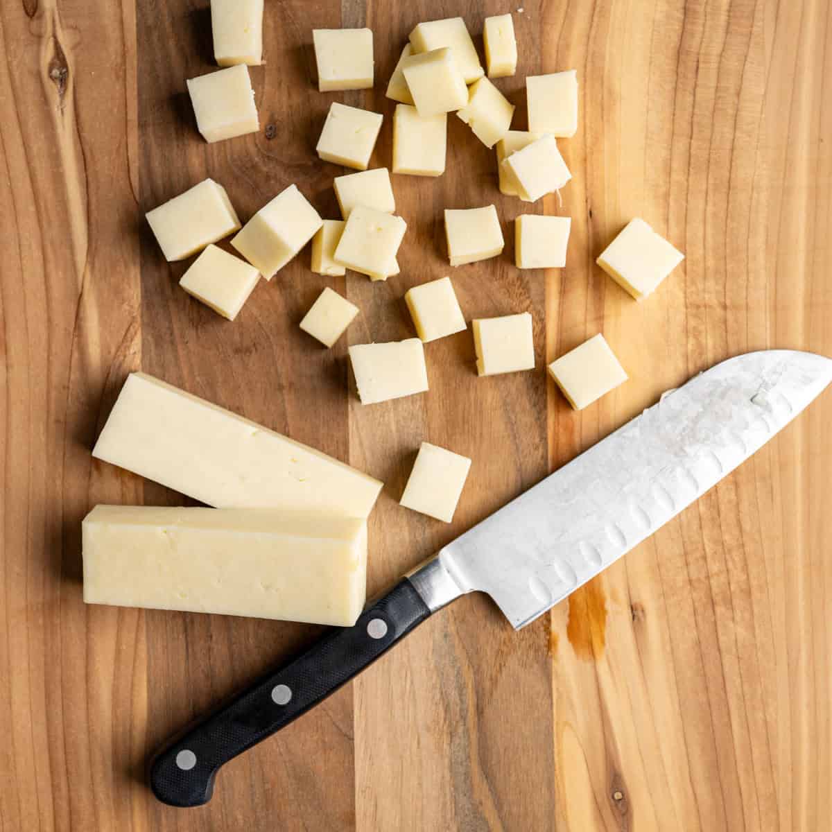 cubed cheese on a wooden cutting board with a knife.