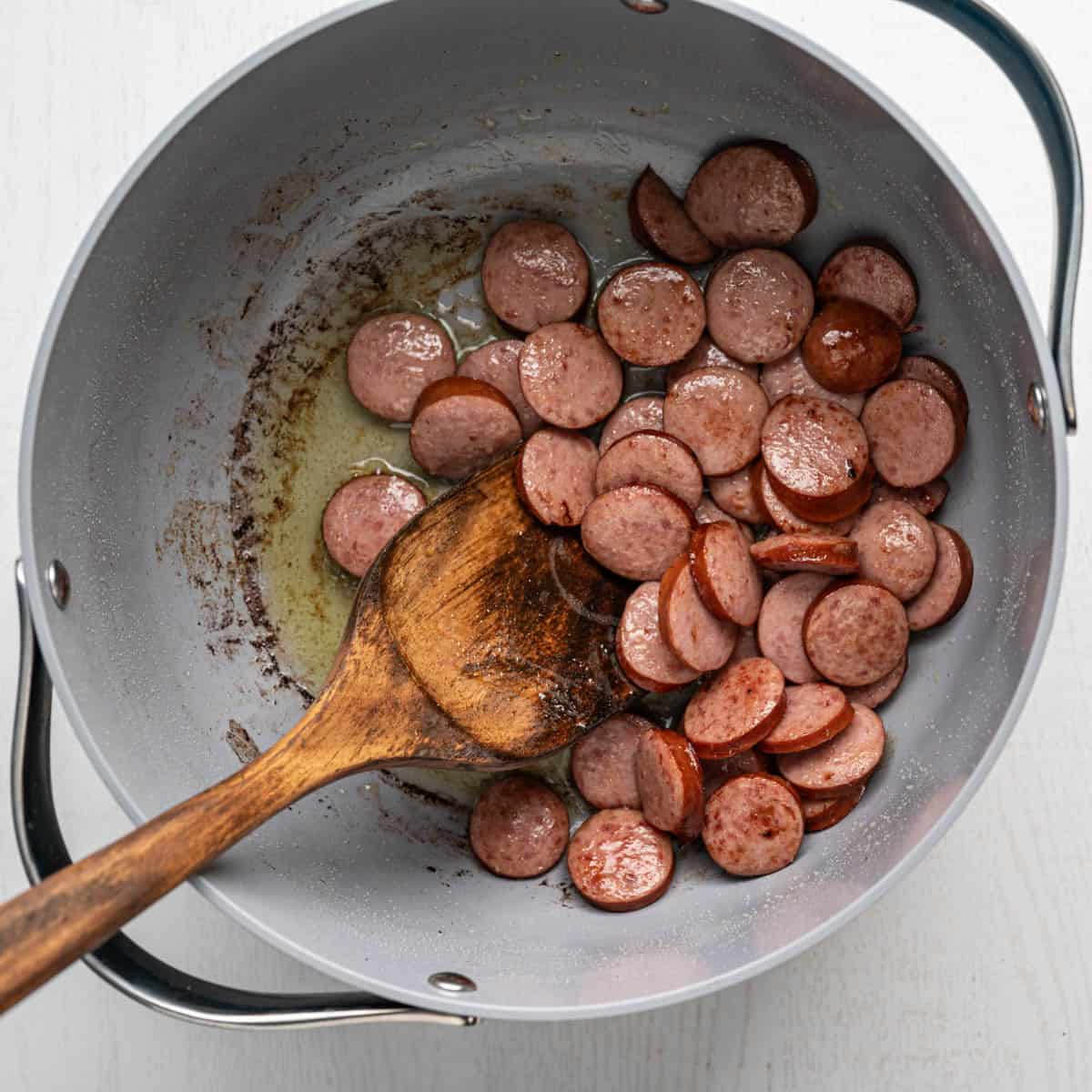cooked sausage in a large pot with a wooden spoon.