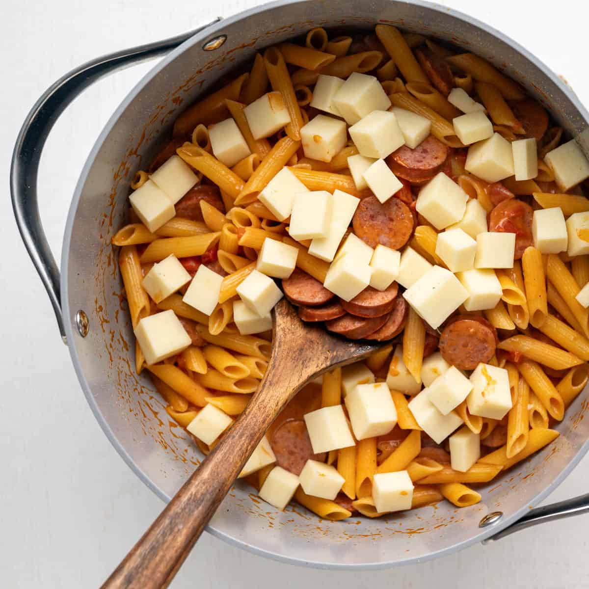 cubed cheese added to the cooked pasta in a large pot.