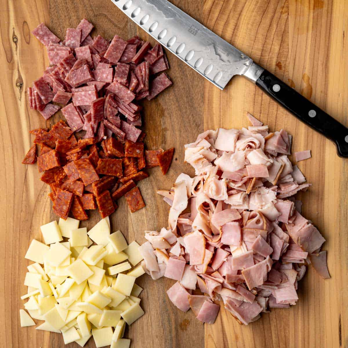 the deli meats and provlone cheese chopped on a wooden board.