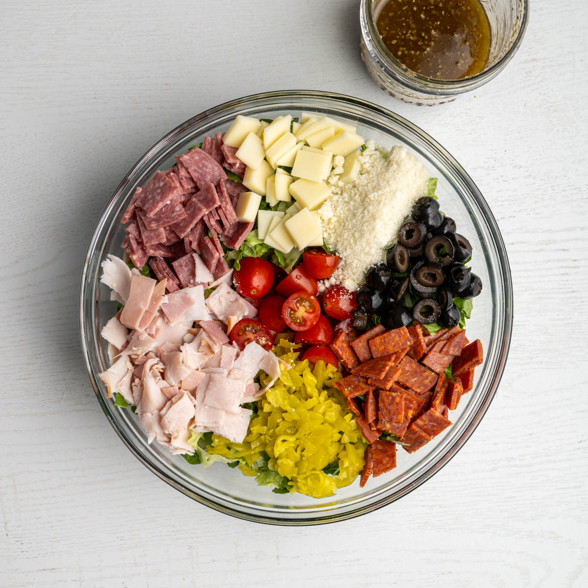 a glass bowl filled with all the ingredients alongside a mason jar of homemade dressing.