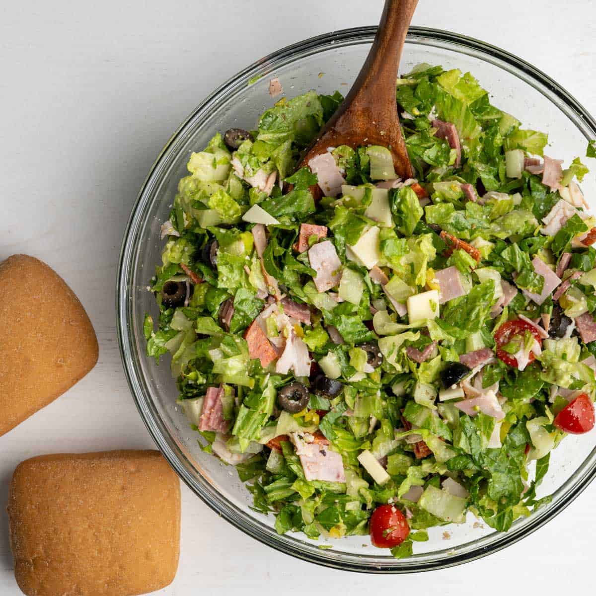 chopped salad in a large glass bowl alongside two gluten free buns.