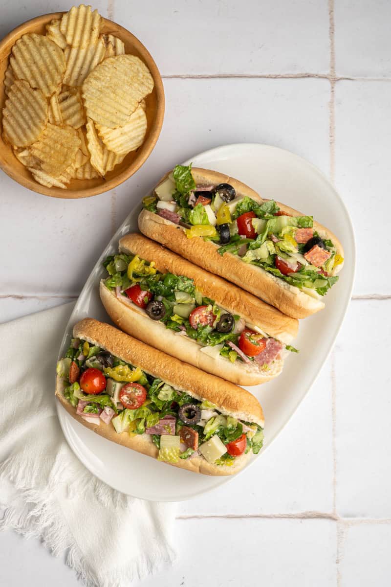 three chopped sandwiches on a white platter with a small bowl of plain chips.