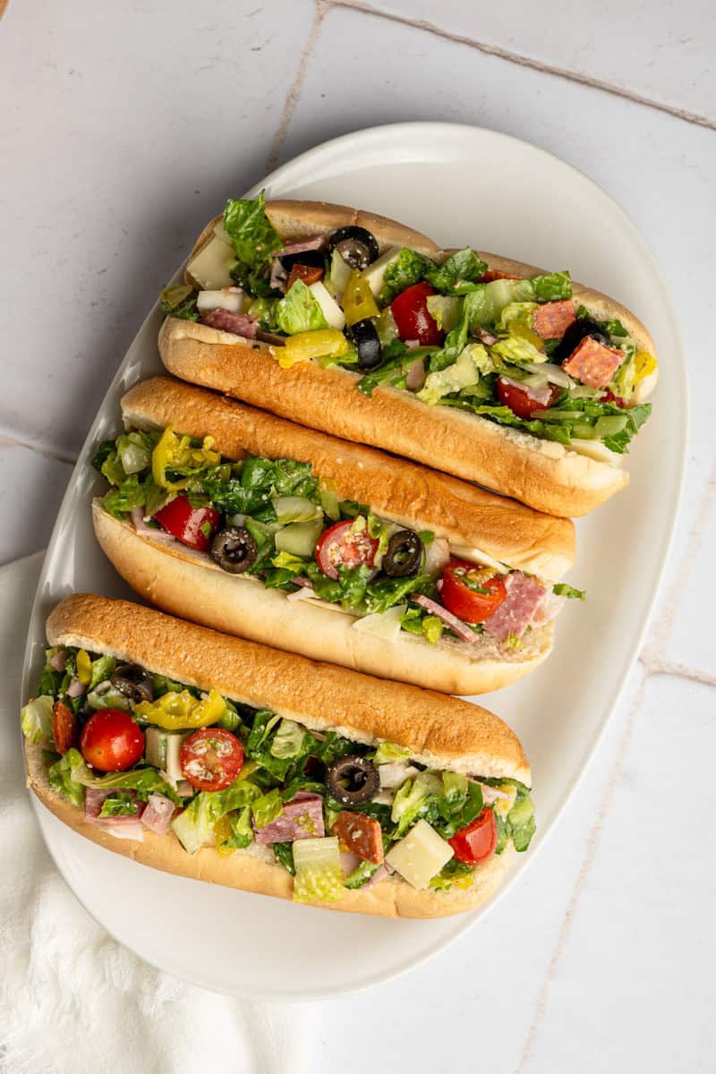 three chopped Italian sandwiches on a white platter.