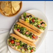 three chopped Italian sandwiches on a white platter with a bowl of chips.