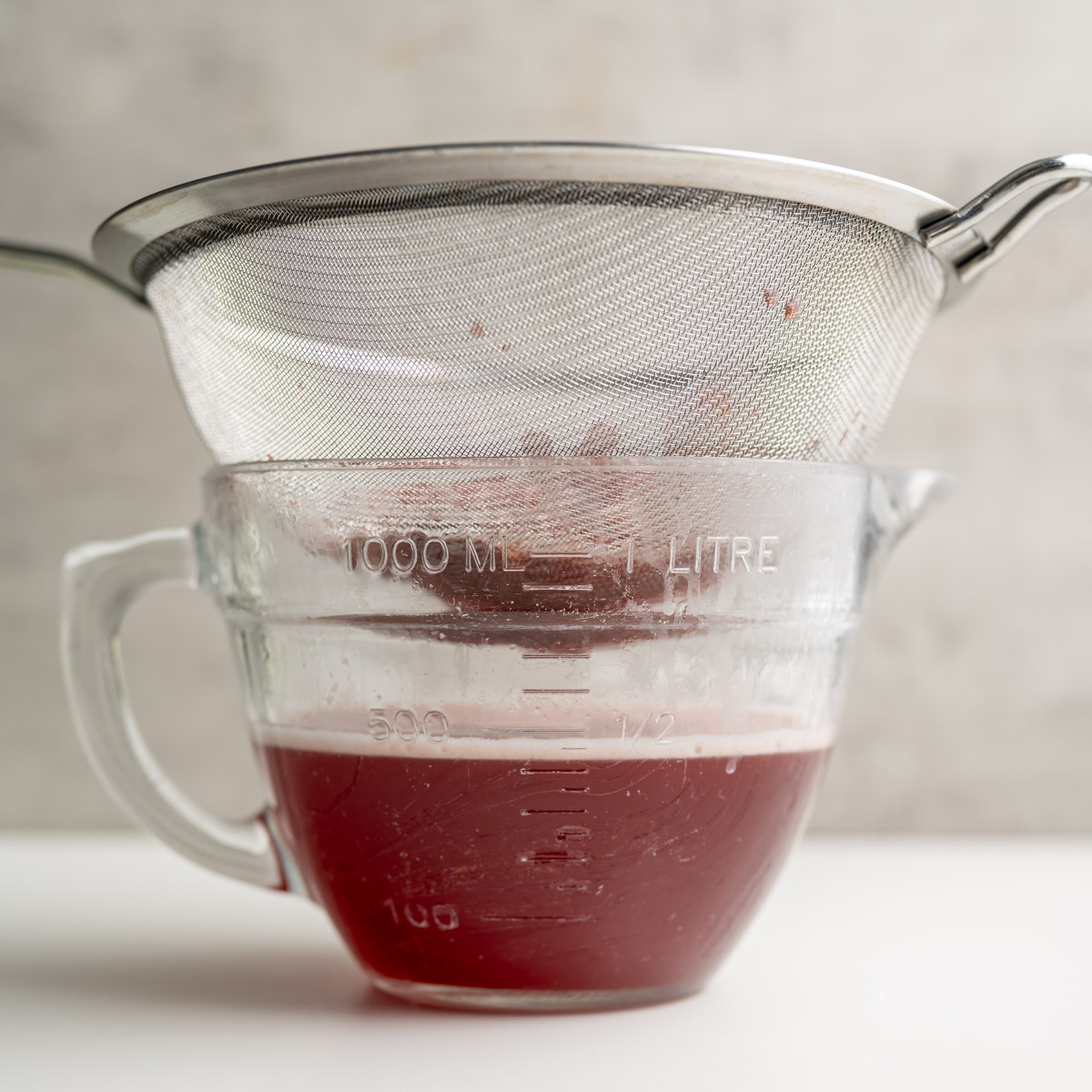 straining the cooked strawberry simple syrup in a fine mesh strainer witha glass bowl below.