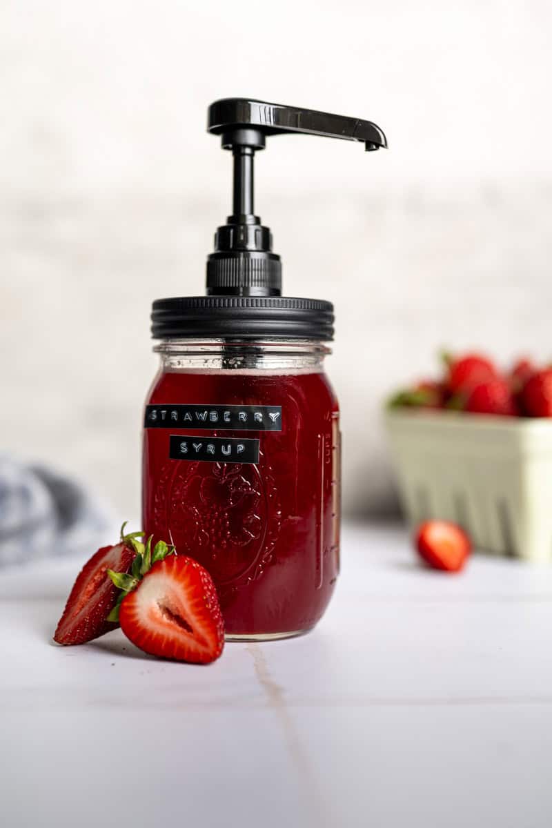 mason jar with pump filled with strawberry syrup alongside sliced strawberries.
