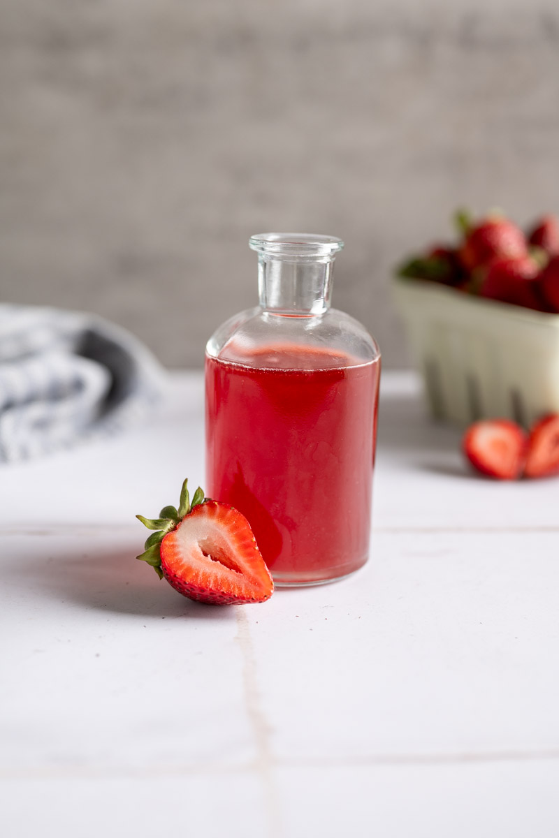 glass jar filled with strawberry syrup alongside fresh strawberries.