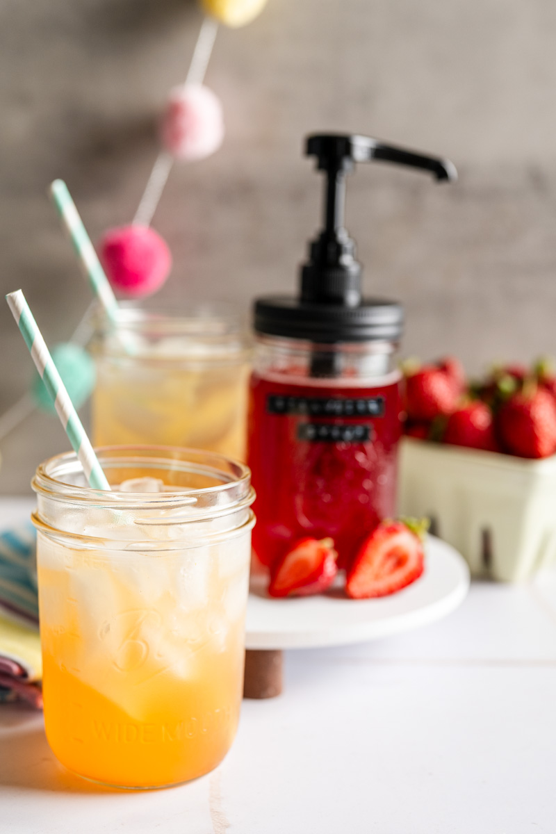 strawberry syrup in a mason jar alongside two glasses of lemonade with syrup.
