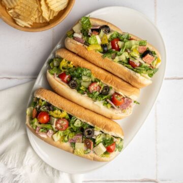three chopped italian sandwiches on a platter with a side of plain chips.