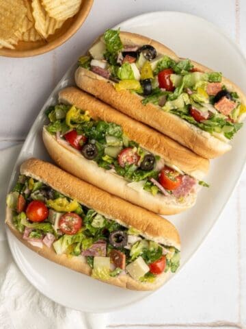 three chopped italian sandwiches on a platter with a side of plain chips.
