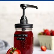 mason jar filled with strawberry syrup with a pump and label alongside fresh strawberries.