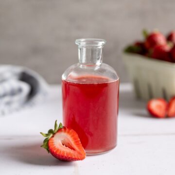 pretty glass gar filled with strawberry syrup alongside a sliced strawberry.