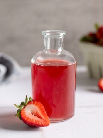 pretty glass gar filled with strawberry syrup alongside a sliced strawberry.