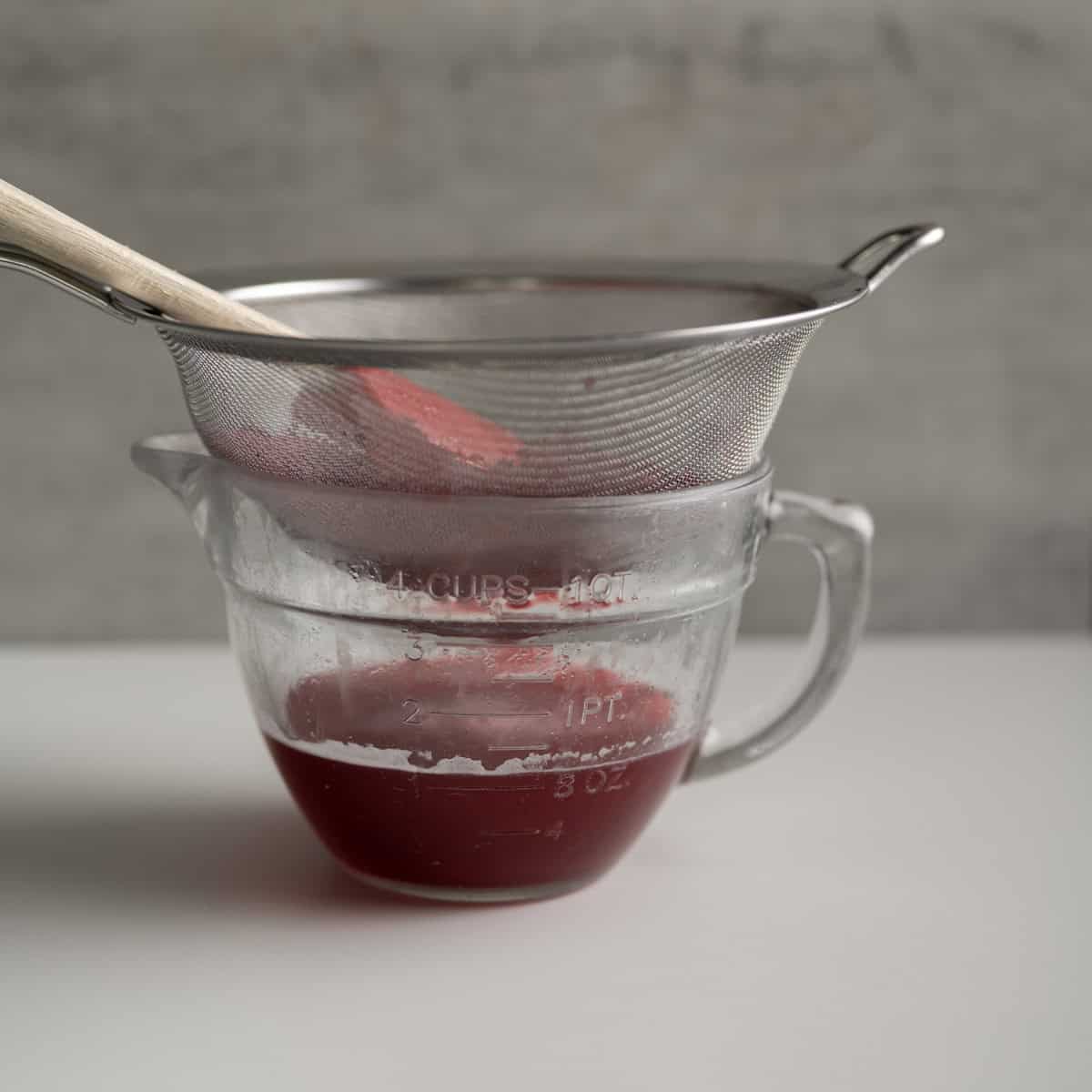cooked rhubarb in a fine mesh strainer with a glass bowl catching it below.