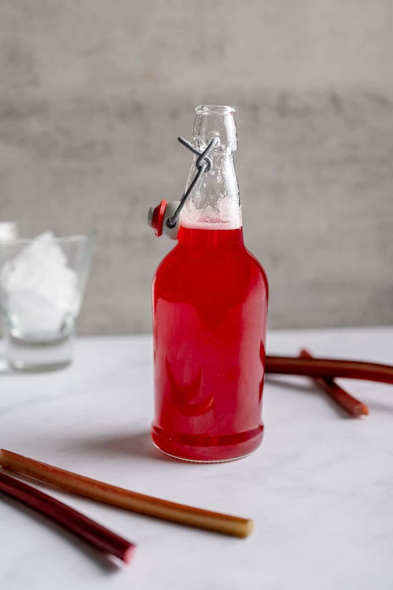 jar of rhubarb syrup alongside fresh rhubarb stalks.